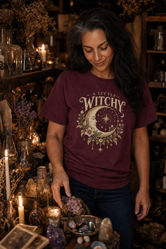 Woman browsing a candlelit vintage crystal shop wearing the maroon A Little Witchy tee