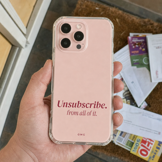 Clear iPhone case printed “Unsubscribe. from all of it.” in dark rose, held over a pile of junk mail