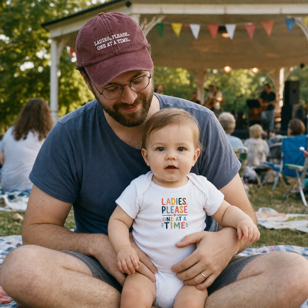 Ladies, Please. One at a Time. matching set: dad in the maroon vintage cap, baby in the Colour Edition bodysuit, at a park concert